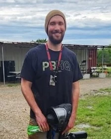 Trevor Convirs at a paintball field holding his mask and marker